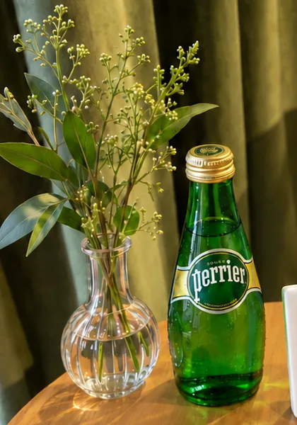 Perrier and a small vase of greenery beside the green velvet curtain in Suite 48